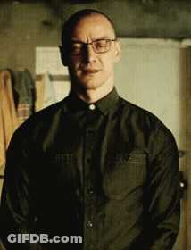 A Man Wearing Glasses And A Black Shirt Is Standing In A Room GIF