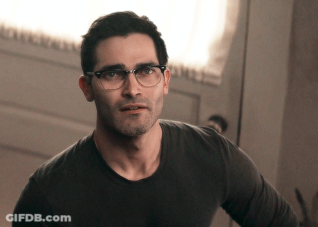 A Man Wearing Glasses And A Black Shirt Is Standing In Front Of A Door GIF