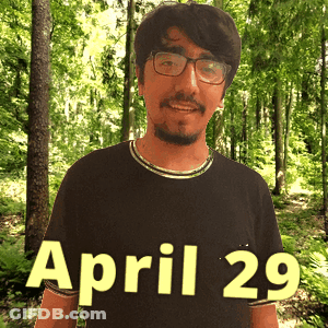 A Man Wearing Glasses And A Black Shirt Stands In The Woods On April 29 GIF