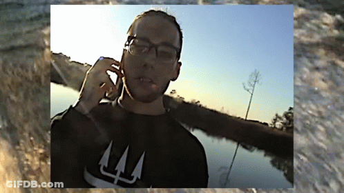 A Man Wearing Glasses And A Black Shirt With The Letter L On It GIF