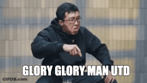 A Man Wearing Glasses And A Black Sweatshirt Says Glory Glory Man Utd In White Letters GIF