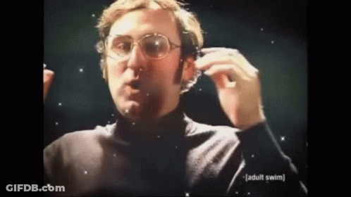A Man Wearing Glasses And A Black Turtleneck Is Holding A Pair Of Headphones . GIF