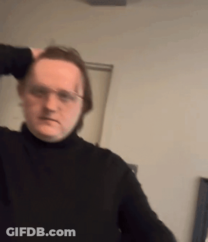 A Man Wearing Glasses And A Black Turtleneck Is Holding His Hair . GIF