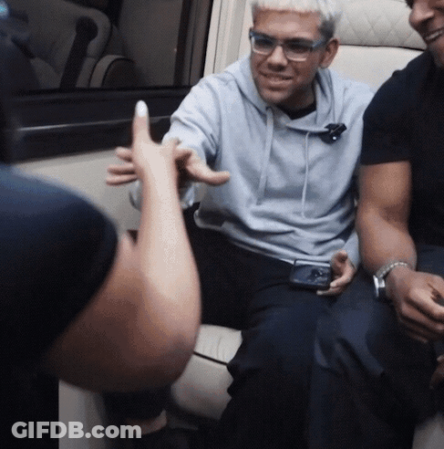 A Man Wearing Glasses And A Blue Hoodie Is Sitting In A Chair GIF