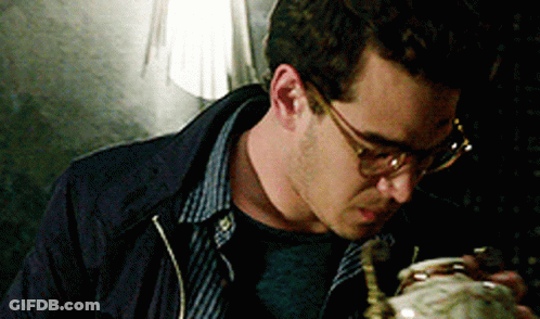A Man Wearing Glasses And A Blue Jacket Is Looking Down At Something GIF