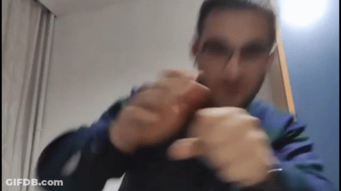A Man Wearing Glasses And A Blue Jacket Is Making A Funny Face While Holding His Hands Together . GIF