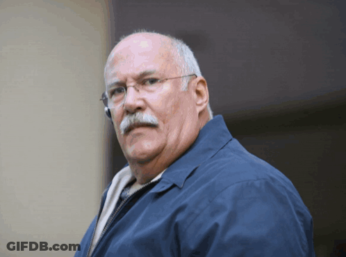 A Man Wearing Glasses And A Blue Jacket Looks At The Camera GIF