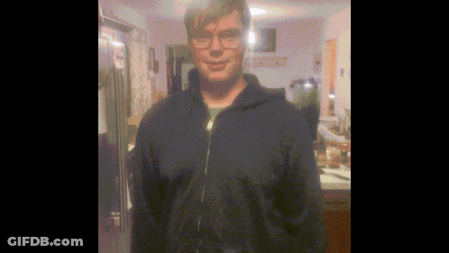 A Man Wearing Glasses And A Blue Jacket Stands In Front Of A Refrigerator GIF