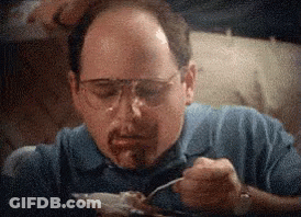 A Man Wearing Glasses And A Blue Shirt Is Eating Food With A Fork . GIF