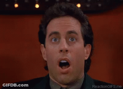 A Man Wearing Glasses And A Blue Shirt Is Laughing With His Mouth Open . GIF