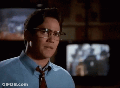 A Man Wearing Glasses And A Blue Shirt Is Looking At Something GIF