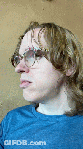 A Man Wearing Glasses And A Blue Shirt Is Making A Face GIF