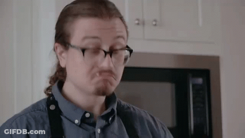 A Man Wearing Glasses And A Blue Shirt Is Making A Funny Face In Front Of A Microwave . GIF
