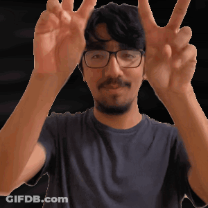 A Man Wearing Glasses And A Blue Shirt Is Making A Peace Sign GIF