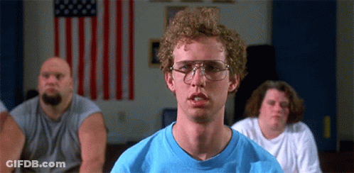 A Man Wearing Glasses And A Blue Shirt Is Sitting In Front Of A Flag . GIF