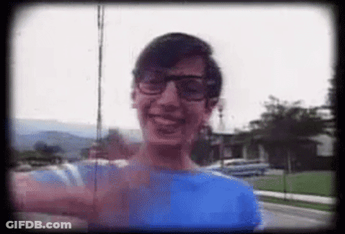 A Man Wearing Glasses And A Blue Shirt Is Smiling In A Video . GIF