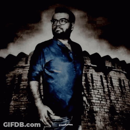 A Man Wearing Glasses And A Blue Shirt Is Standing In Front Of A Brick Wall With The Hashtag Nagkarism GIF