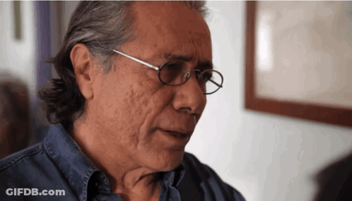 A Man Wearing Glasses And A Blue Shirt Looks At Something GIF