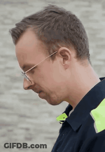 A Man Wearing Glasses And A Blue Shirt Looks Down At Something GIF