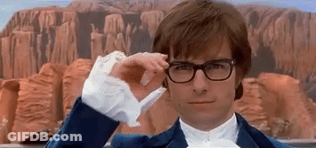 A Man Wearing Glasses And A Blue Suit Is Adjusting His Glasses In Front Of A Mountain . GIF