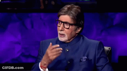 A Man Wearing Glasses And A Blue Suit Is Sitting In Front Of A Purple Wall . GIF