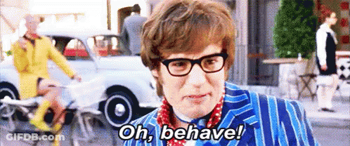 A Man Wearing Glasses And A Blue Suit Is Standing On A Street And Says `` Oh , Behave ! '' GIF