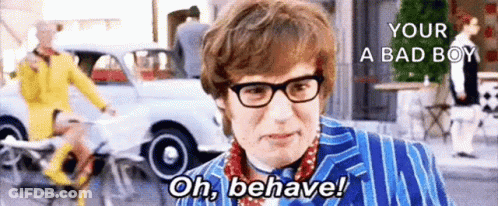 A Man Wearing Glasses And A Blue Suit Is Standing On A Street With A Car In The Background . GIF