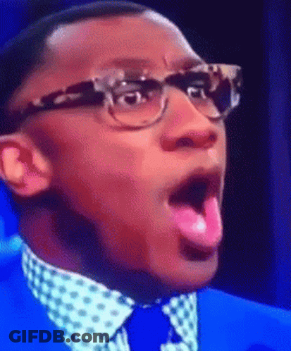 A Man Wearing Glasses And A Blue Suit Is Sticking Out His Pink Tongue GIF