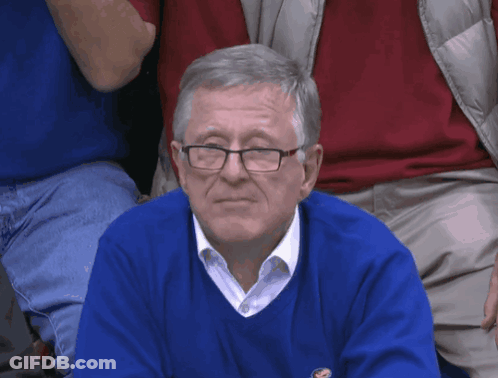 A Man Wearing Glasses And A Blue Sweater Is Sitting In The Audience GIF