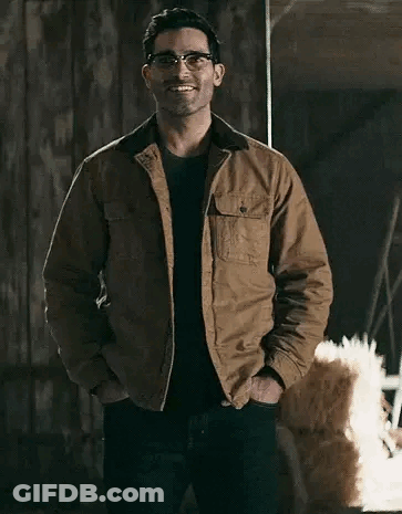 A Man Wearing Glasses And A Brown Jacket Is Standing In A Room With His Hands In His Pockets . GIF