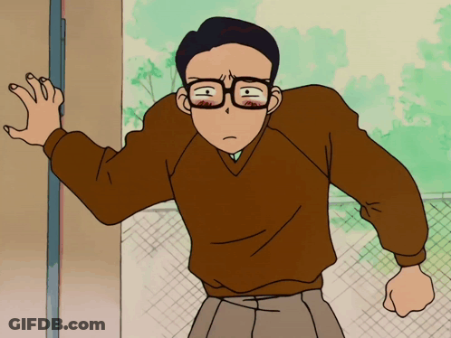 A Man Wearing Glasses And A Brown Sweater Stands In Front Of A Door GIF