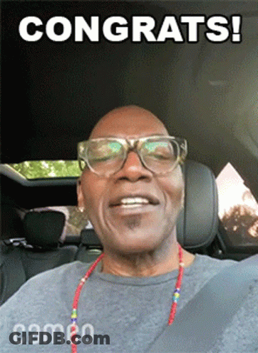 A Man Wearing Glasses And A Cameo Necklace Is Smiling GIF