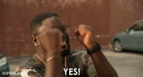 A Man Wearing Glasses And A Camouflage Shirt Is Holding His Fist Up And Saying Yes . GIF