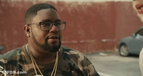 A Man Wearing Glasses And A Camouflage Shirt Is Standing In A Parking Lot . GIF