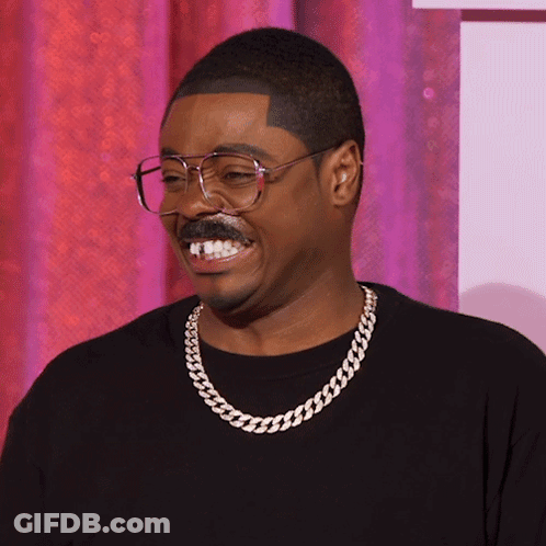 A Man Wearing Glasses And A Chain Around His Neck Is Smiling GIF