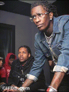 A Man Wearing Glasses And A Denim Jacket Is Standing In A Crowd GIF