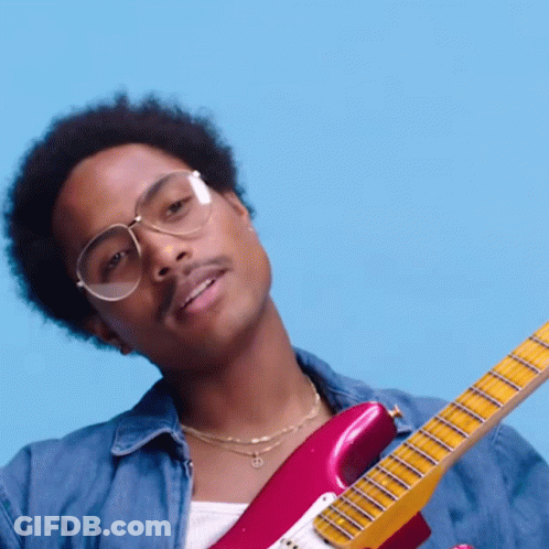 A Man Wearing Glasses And A Denim Shirt Is Holding A Pink Guitar GIF