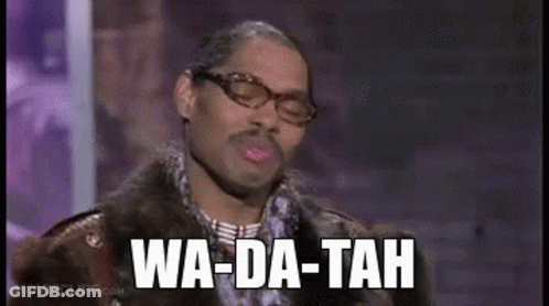 A Man Wearing Glasses And A Fur Coat Is Standing In Front Of A Microphone . GIF