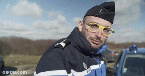 A Man Wearing Glasses And A Gendarmerie Uniform Looks At The Camera GIF