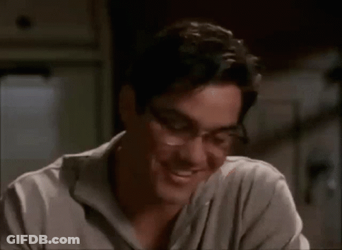 A Man Wearing Glasses And A Gray Shirt Smiles GIF