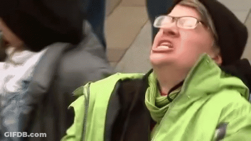 A Man Wearing Glasses And A Green Jacket Is Sitting On A Train . GIF