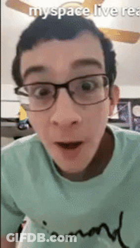 A Man Wearing Glasses And A Green Shirt Is Looking At The Camera . GIF