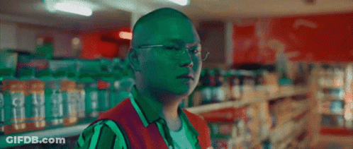 A Man Wearing Glasses And A Green Vest Is In A Store GIF
