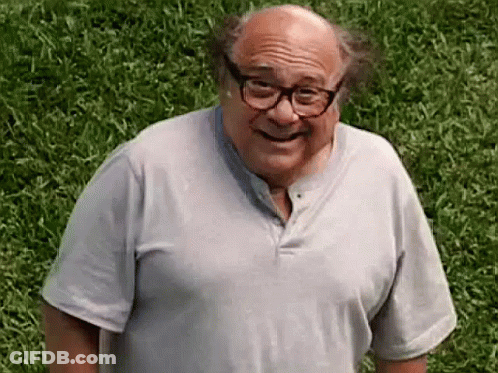 A Man Wearing Glasses And A Grey Shirt Is Standing In The Grass . GIF