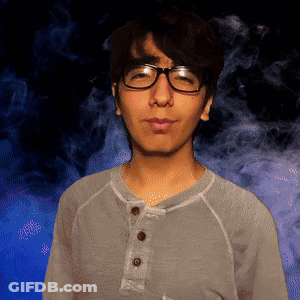 A Man Wearing Glasses And A Grey Shirt Stands In Front Of Smoke GIF