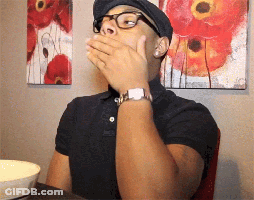 A Man Wearing Glasses And A Hat Is Covering His Mouth GIF