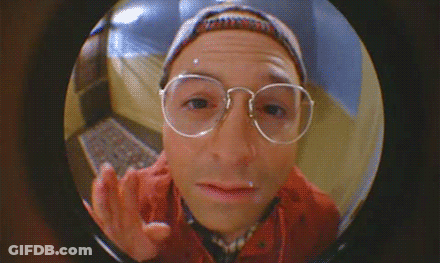 A Man Wearing Glasses And A Hat Is Looking Through A Door GIF