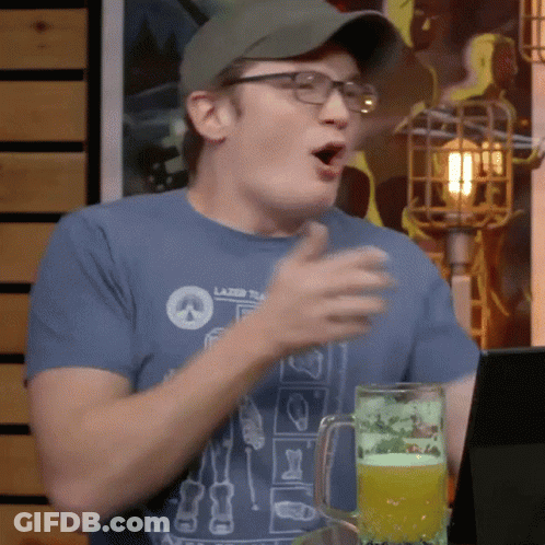 A Man Wearing Glasses And A Hat Is Sitting At A Table With A Glass Of Beer . GIF
