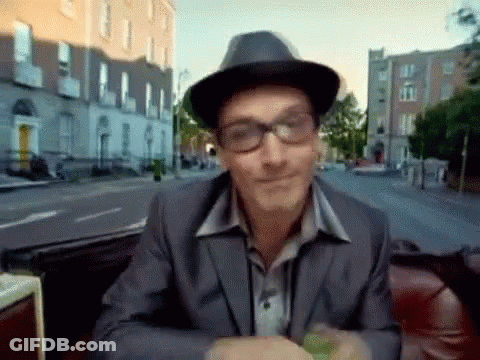 A Man Wearing Glasses And A Hat Is Sitting On A Red Couch GIF