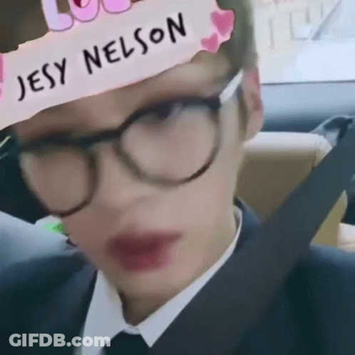 A Man Wearing Glasses And A Hat With The Name Jesy Nelson On It Is Sitting In A Car . GIF